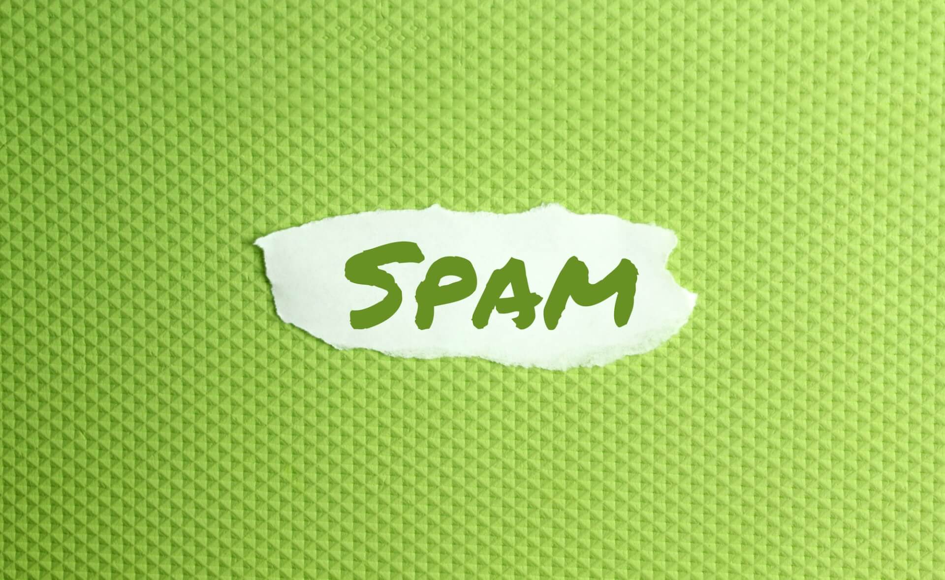 a torn paper written with inscription spam on a green background